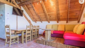 A cozy room with a wooden ceiling, a dining table with chairs, and a colorful sofa. - LA Ferme DU Soleil - Combles (ALBIEZ MONTROND)