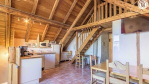 A rustic kitchen with wooden beams, a dining area with a wooden table and chairs, and a staircase leading to an upper level. - LA Ferme DU Soleil - Combles (ALBIEZ MONTROND)