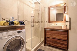 A modern bathroom with a glass-enclosed shower, a wooden vanity with a mirror, and a front-loading washing machine.