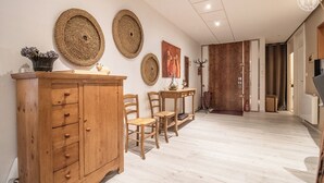 En gang med et træskab, vægdekorationer i flet og et spiseområde med træstole og et bord.