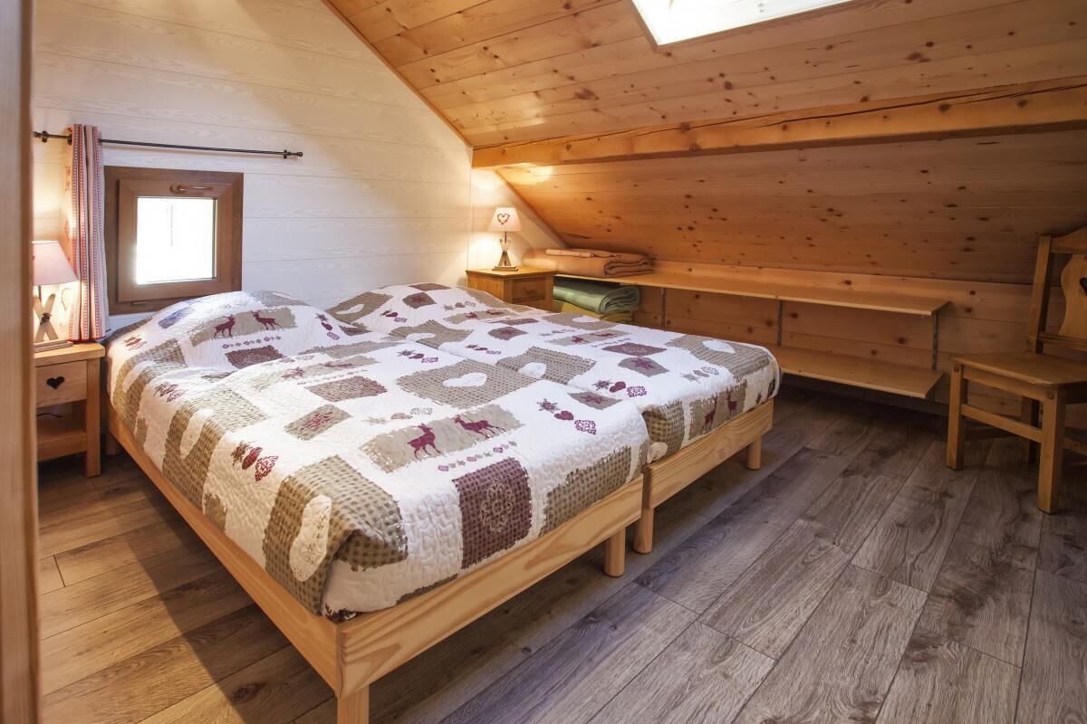 A cozy attic bedroom with a wooden bed, a small bedside table, a lamp, and a window with curtains.