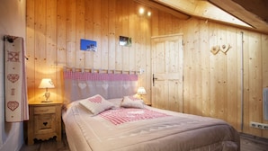 A wooden-paneled bedroom with a bed, two bedside lamps, a nightstand, and a wall-mounted heater. - Chalet DES Alpes - Val-cenis (VAL CENIS)