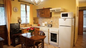 Una cocina compacta con una mesa de comedor, armarios de madera, un microondas, un refrigerador y una lavadora.