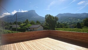 Eine Holzterrasse mit Blick auf einen Berg und ein kleines Haus im Hintergrund.
