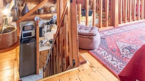 A wooden interior with a staircase, a kitchen area, and a red patterned rug. - LES Mesanges - Jarrier (JARRIER)