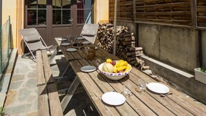 A wooden patio table with a beige umbrella, surrounded by chairs and a bowl of fruit. - Chez LE Marquis DU Pontet 4 (VALLOIRE)