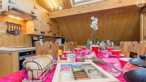A cozy kitchen with wooden cabinets, a bread rack, and a dining table set with red dishes and a pink tablecloth. - LA Grange Neuve - Frontenex (FRONTENEX)