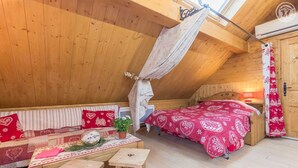 A cozy attic bedroom with a wooden ceiling, a canopy bed, a sofa with patterned cushions, and a small table with a plant. - LA Grange Neuve - Frontenex (FRONTENEX)