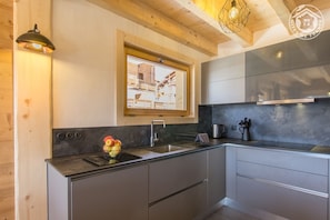 Uma cozinha moderna com fogão embutido, janela com vista para uma área residencial e luminária pendente.