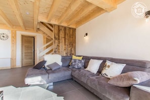 Uma sala de estar moderna com um sofá modular cinza, uma escada de madeira e uma porta branca.