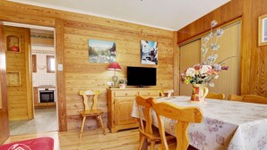 Una habitación acogedora con paredes de madera, una mesa de comedor con sillas, un televisor y un jarrón de flores.