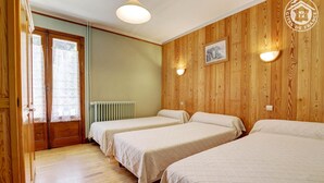 Una habitación con tres camas, paredes de madera, un radiador y una ventana con cortinas.