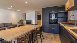 A modern kitchen with dark cabinets, a wooden dining table, and a built-in oven.