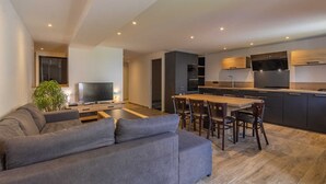 A modern living room with a grey sofa, a TV, and a dining area with wooden chairs and a table.