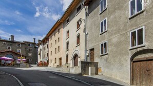 A street view of a building with multiple windows and a wooden door. There are outdoor seating areas with umbrellas.