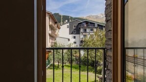 A balcony with a stone wall and a metal railing, overlooking a green garden and buildings in the background.
