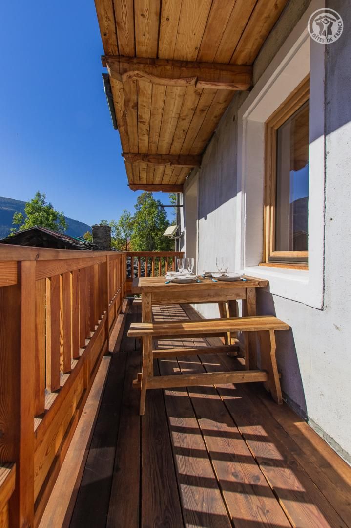 Une terrasse en bois avec une table et des bancs, une fenêtre et une vue sur les montagnes.