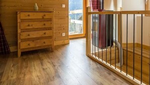 Un interior de madera con un aparador de madera, un cuadro en la pared y vistas a través de una puerta.