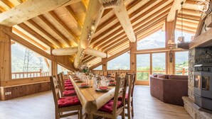 A wooden dining area with a high ceiling, large windows, and a stone fireplace. - Chalet Villaroger - LA Perle DES Neiges (VILLAROGER)