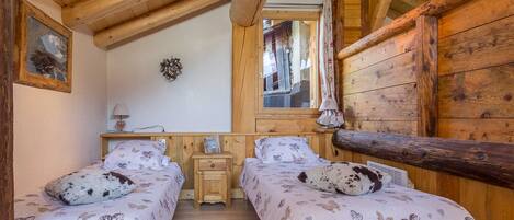A cozy room with two beds, wooden walls, a mirror, and a small bedside table with a lamp.