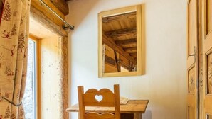 A wooden dining table with a heart-shaped backrest, a mirror on the wall, and a window with curtains. - Chalet Villaroger - LA Perle DES Neiges (VILLAROGER)