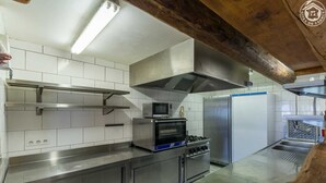 A commercial kitchen with stainless steel appliances, white tiled walls, and a wooden ceiling beam. - Chalet Villaroger - LA Perle DES Neiges (VILLAROGER)