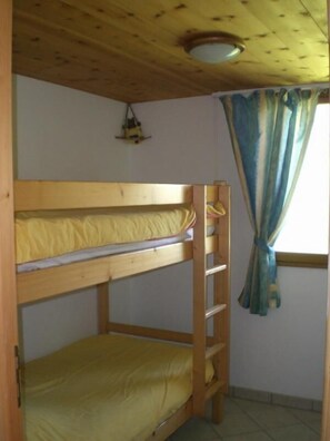 Een slaapkamer met een stapelbed, een houten plafond en een raam met gordijnen.