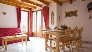 Une pièce chaleureuse avec un plafond en bois, un canapé rouge, une table à manger en bois avec des chaises, et une fenêtre ornée de rideaux rouges.