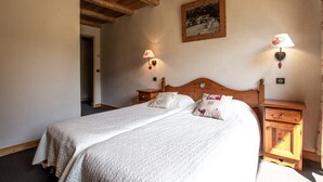 A double bed with a wooden headboard, two bedside tables with lamps, a framed picture on the wall, and a door leading to another room. - LA Pastourelle 2 - Bonneval SUR ARC (BONNEVAL SUR ARC)