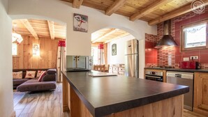 A modern kitchen with wooden cabinets, a central island, and a dining area with a sofa. - LA Pastourelle 2 - Bonneval SUR ARC (BONNEVAL SUR ARC)