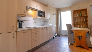 A modern kitchen with wooden cabinets, a microwave, and a dining area with a wooden table and chairs. - Merlin - Ste-helene-du-lac (SAINTE HELENE DU LAC)