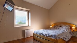 A bedroom with a wooden bed, a window with a view, a wall-mounted TV, and a bedside lamp. - Merlin - Ste-helene-du-lac (SAINTE HELENE DU LAC)