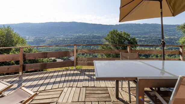 A wooden deck with a table and chairs, an umbrella, and a view of a forested valley. - Merlin - Ste-helene-du-lac (SAINTE HELENE DU LAC)