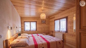 Dormitorio de cabaña de madera con dos camas, una araña y ventanas con cortinas.