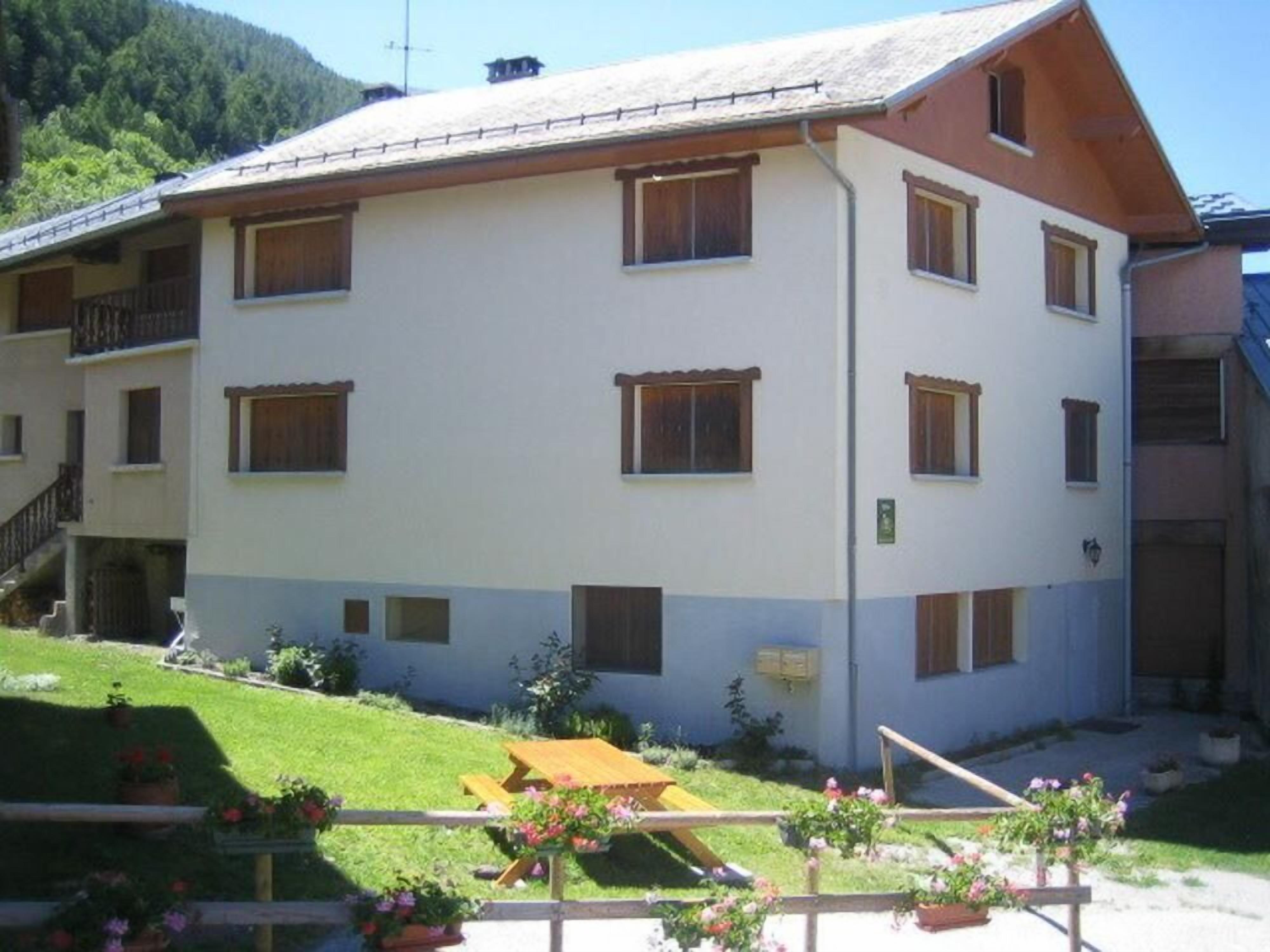 A multi-story building with a flat roof, multiple windows, and a small outdoor seating area with flowers.