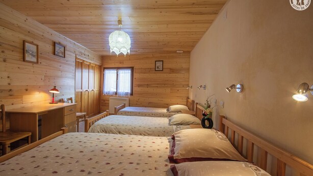 Una habitación acogedora con paredes y techo de madera, dos camas con ropa de cama floral, un escritorio con lámpara y una lámpara colgante.