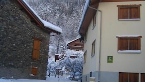 Un pueblo cubierto de nieve con edificios de piedra y madera, una calle estrecha y una montaña al fondo.