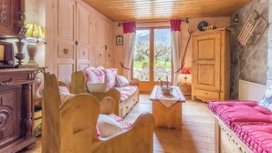 Une pièce chaleureuse, meublée de bois, avec un canapé, une table et une vue sur un jardin, visible à travers une porte vitrée.