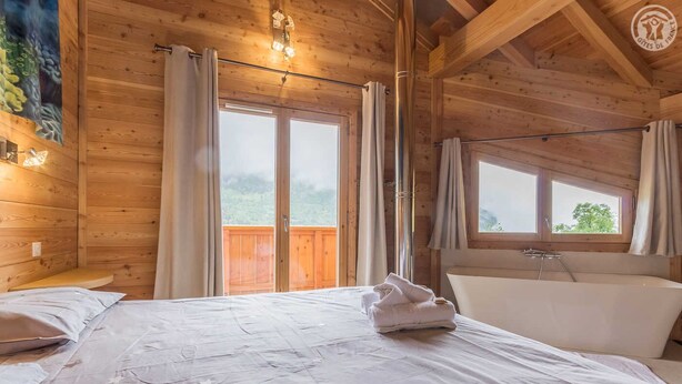 A wooden cabin room with a bed, a bathtub, and large windows. - Chalet Aline - Meribel-les-allues (MERIBEL LES ALLUES)