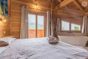 Una habitación de cabaña de madera con cama, bañera y ventanas amplias.