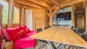 A wooden interior with a large dining table, red sofa, and a TV in the background. - Chalet Aline - Meribel-les-allues (MERIBEL LES ALLUES)