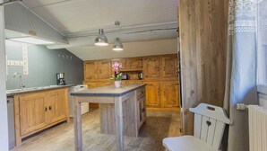 A modern kitchen with wooden cabinets, a central island, pendant lighting, and a white chair. - LE Boujou - Hauteluce-les-saisies (HAUTELUCE LES SAISIES)