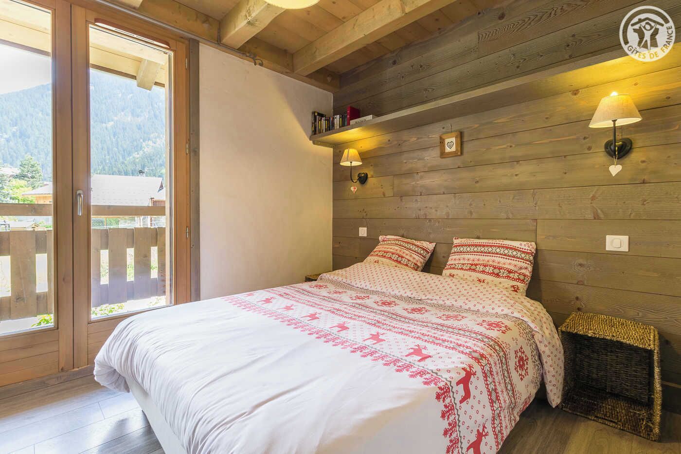 Un dormitorio con cabecera de madera, cama con ropa de cama estampada, mesita de noche, lámpara y vistas al exterior a través de una puerta corredera.