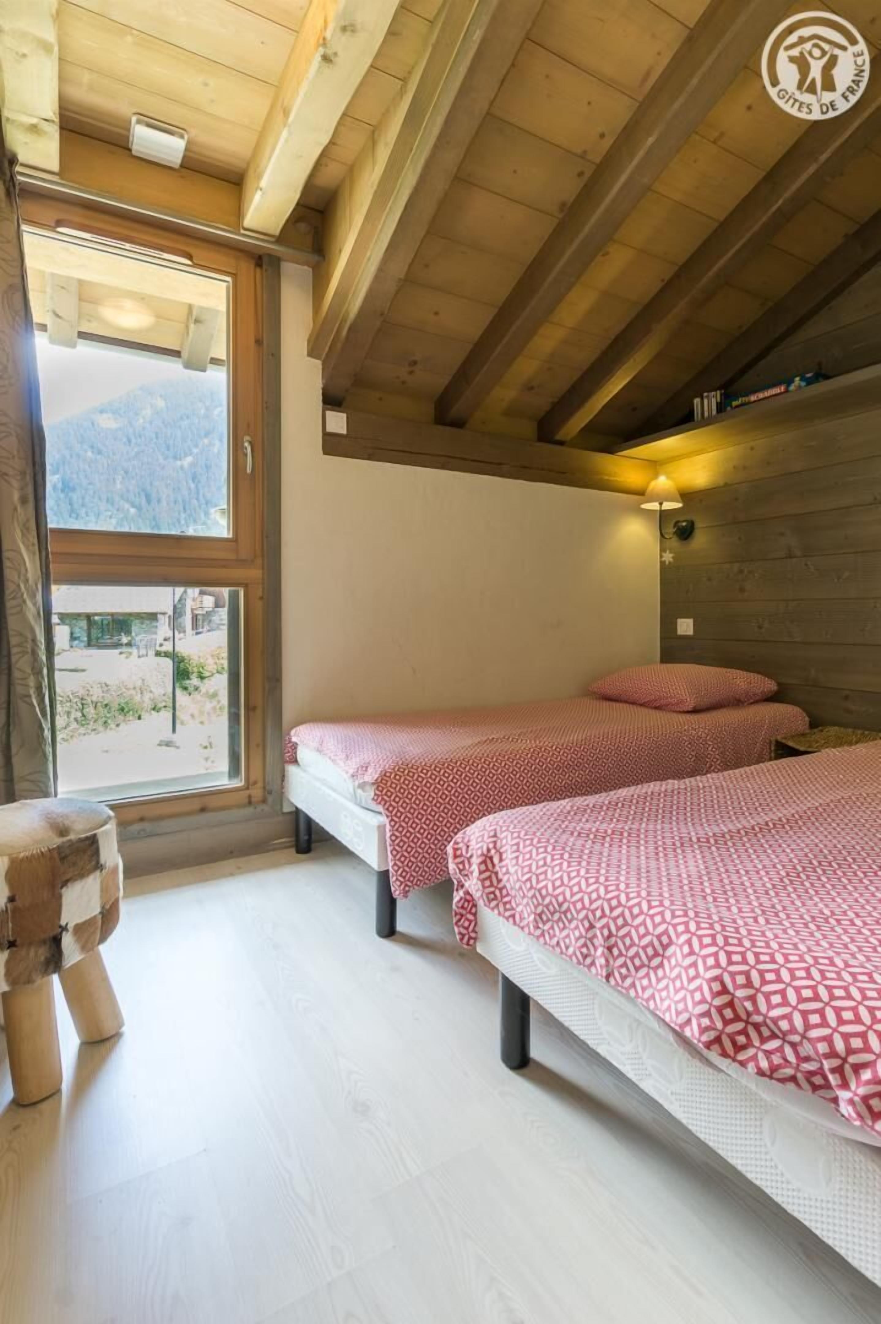 Een kamer met twee bedden, houten balken, een raam met uitzicht op bergen en een klein houten krukje.