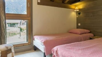 Een kamer met twee bedden, houten balken, een raam met uitzicht op bergen en een klein houten krukje.