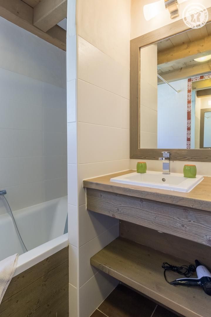 Een badkamer met een badkuip, een houten wastafelmeubel met een spiegel en een handdoekhouder.
