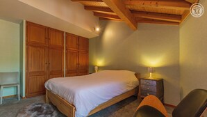 Un dormitorio con una cama de madera, dos mesitas de noche con lámparas, una silla y un armario.