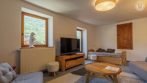Una sala de estar acogedora con televisor, sofá, mesa de centro de madera y ventana con vistas a la vegetación.