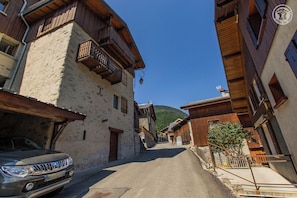 A narrow street with traditional wooden buildings, a parked car, and a clear blue sky.