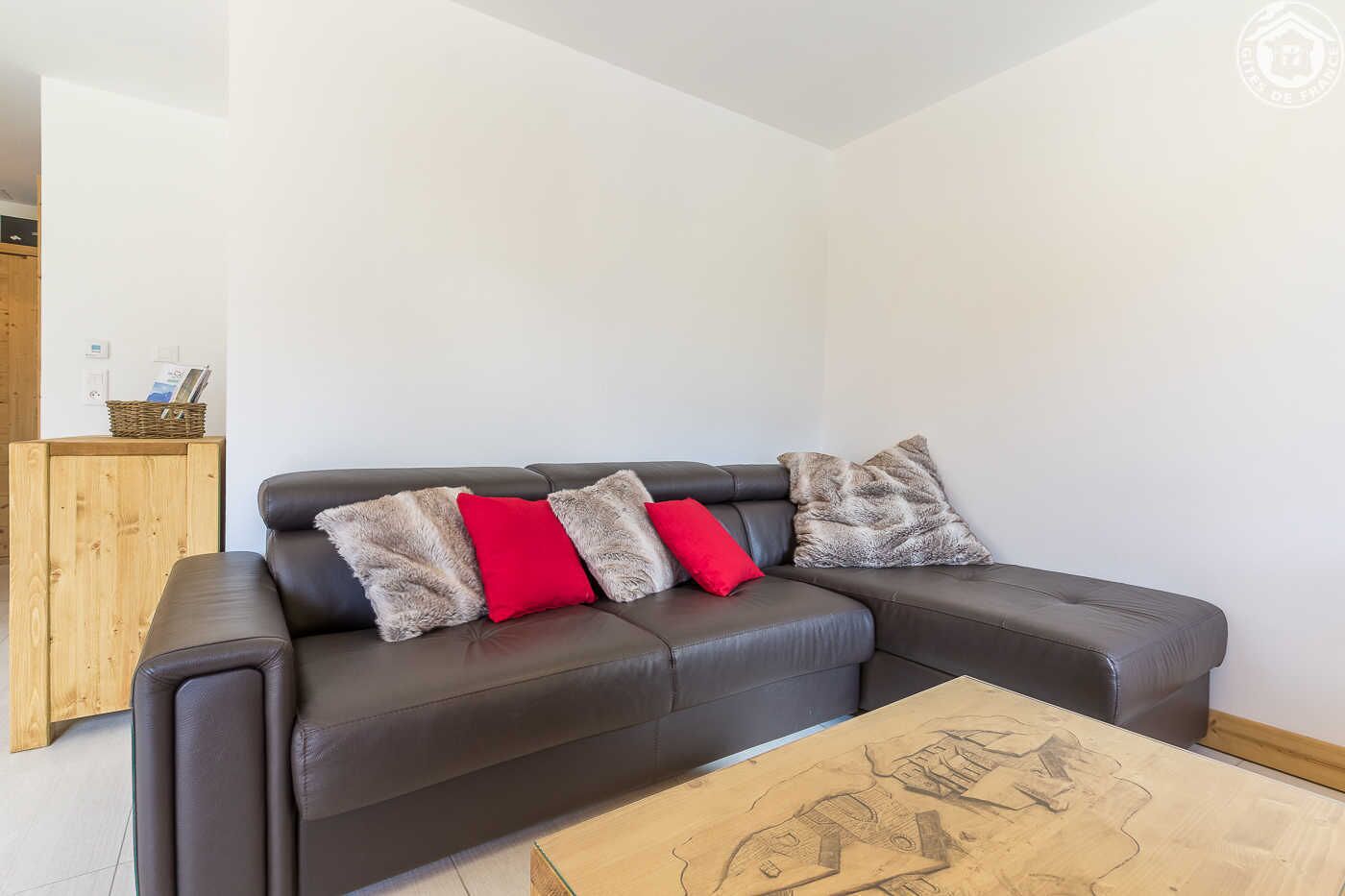 Een moderne woonkamer met een donker leren bank, drie kussens, een houten salontafel met een kaartmotief, en een houten dressoir met een mand en fotolijst.